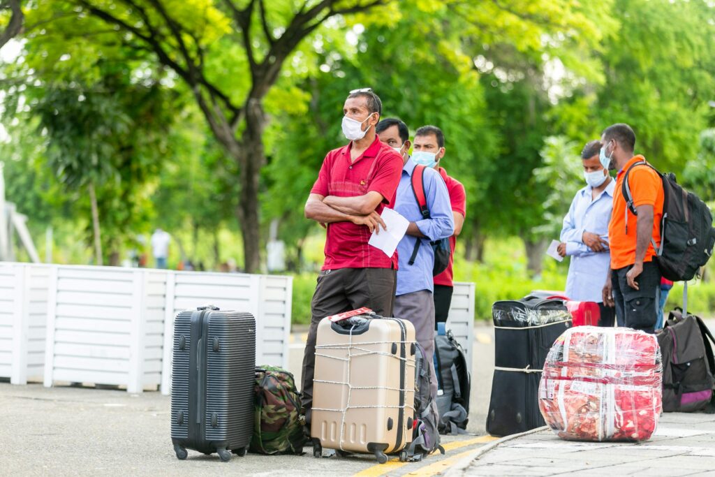 People standing with suitcases wearing masks outdoors, indicative of travel during COVID-19 times.