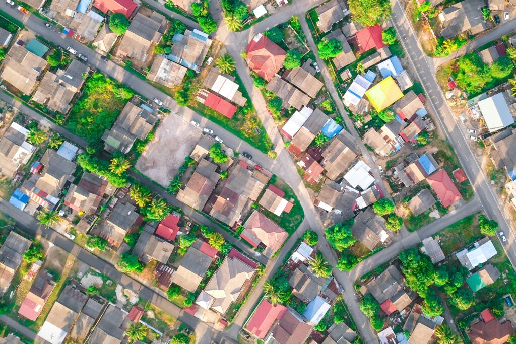 Drone view of small multi colored private houses and verdant trees surrounded by long narrow roads in daylight in summertime