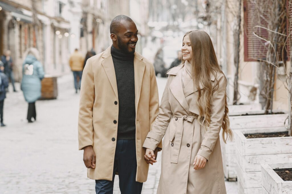 How to Prove a Genuine Relationship for a UK Spouse Visa A joyful multiracial couple holding hands and walking in a winter urban setting.