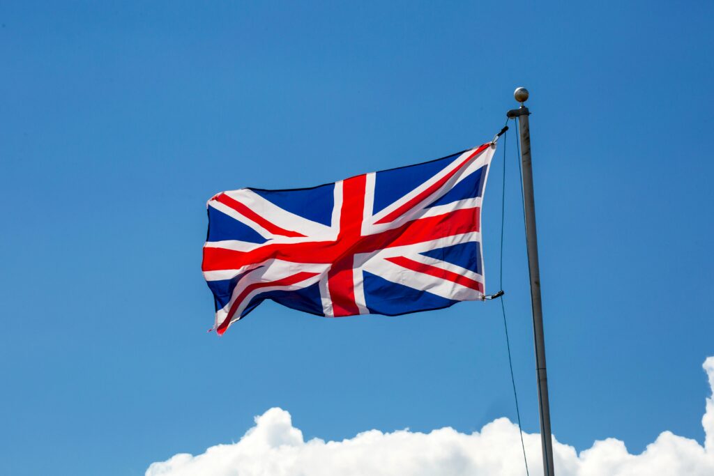 The Union Jack flag of the United Kingdom waving against a clear blue sky.